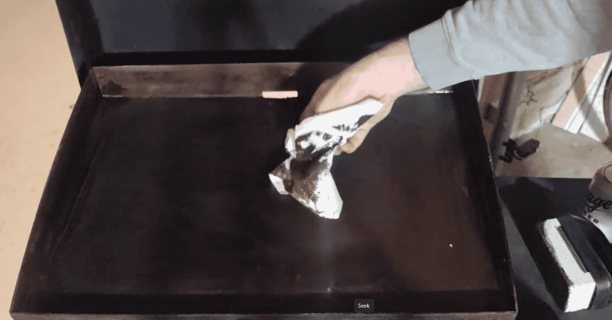 a white paper towel with dirty black grease on it from a blackstone griddle it is wiping down.