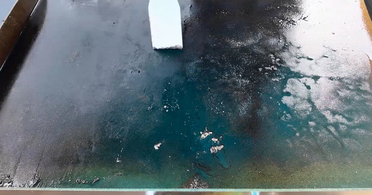 A Blackstone griddle with food debris, grease buildup, and discoloration, being scraped clean with a griddle scraper