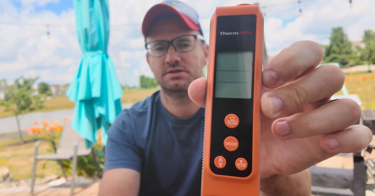 Man holding a ThermoPro infrared thermometer outdoors to demonstrate how to check griddle surface temperature