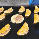 Corn tortillas filled with a seasoned ground beef mixture being cooked and folded into tacos dorados on a Blackstone griddle.