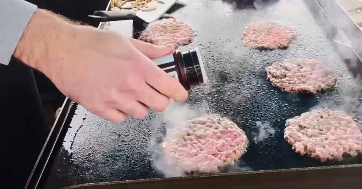 Adding the seasoning to the burgers as they cook.