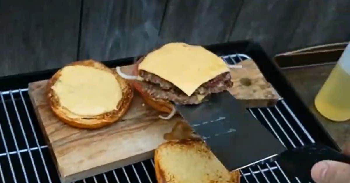 Removing cooked smash burgers with cheese from the griddle.