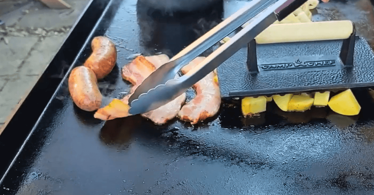 Metal tongs picking up bacon on a griddle.