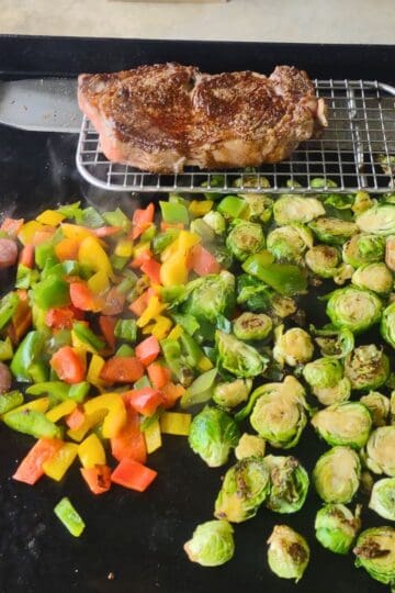 A sizzling steak, diced bell peppers, Brussels sprouts, and crispy roasted potatoes cooking on a Blackstone griddle.