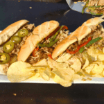 3 cheese steaks sitting on a white plate on a blackstone griddle.