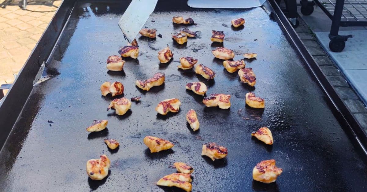 chicken pieces cooking on a blackstone griddle with a spatula