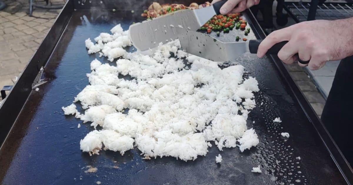 white rice being spread out on a griddle with two spatulas
