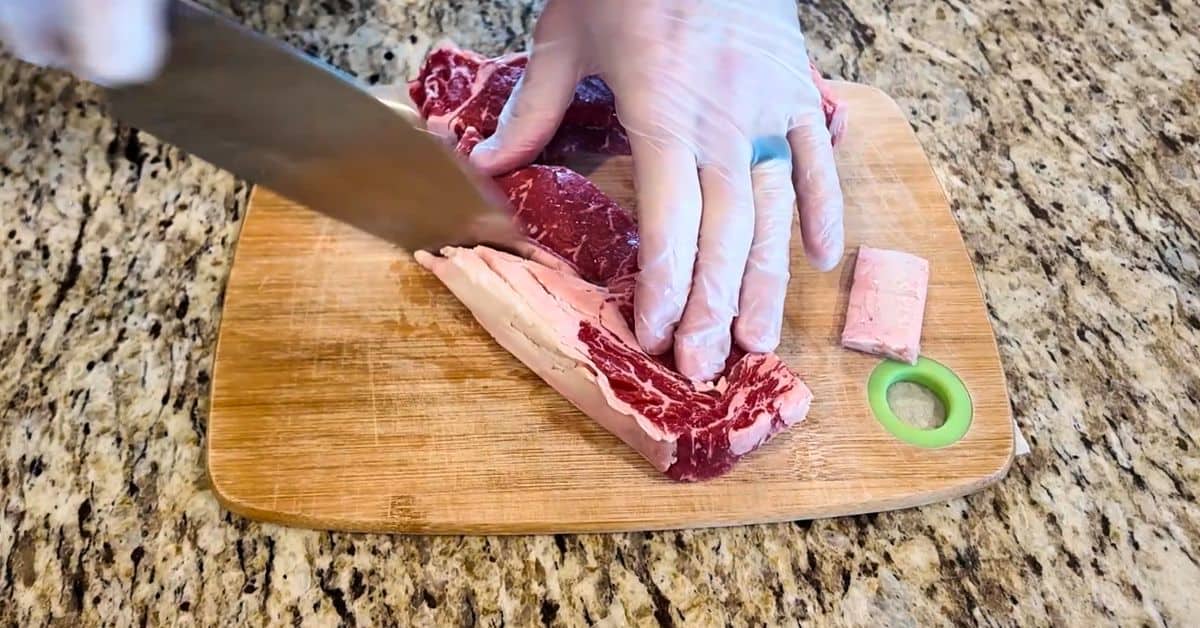 A Ribeye steak with a knife cutting the large fatty pieces out.