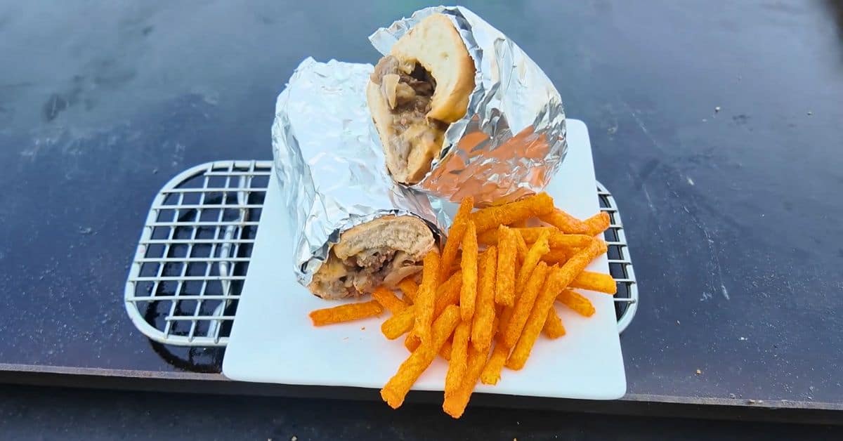 a cheese steak wrapped in foil with andy hot fries on a white plate.