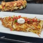 a hash brown omelette on a blackstone griddle on a white plate with salsa and sour cream on top