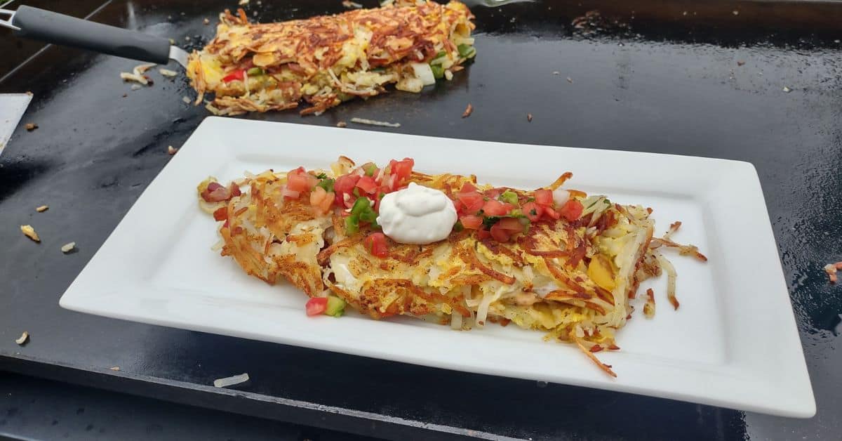 a hash brown omelette on a blackstone griddle on a white plate with salsa and sour cream on top