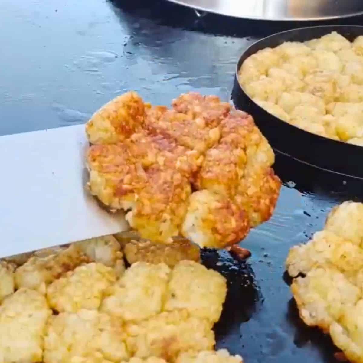 Cripsy puck of tater tots smashed together on a blackstone griddle with more tots in the background.