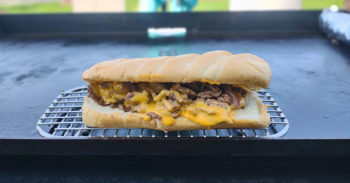 a philly cheese steak on a blackstone griddle with cheese whiz coming of.