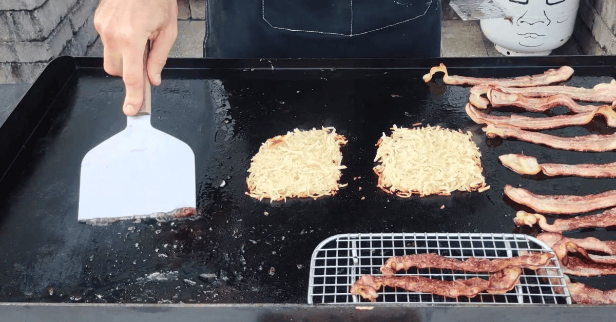 a wide scraper staula bacon hashbrowns on a blackstone griddle.