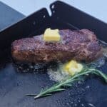 eared steak on a Blackstone griddle topped with melting butter, garlic cloves, and fresh rosemary.