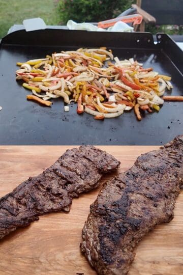 Grilled skirt steak resting on a cutting board with peppers and onions cooking on a Blackstone griddle in the background.