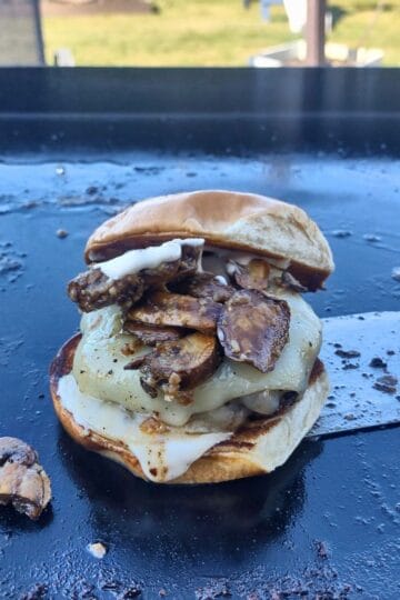 a mushrooms swiss burger sitting on a spatula on a blackstoen griddle